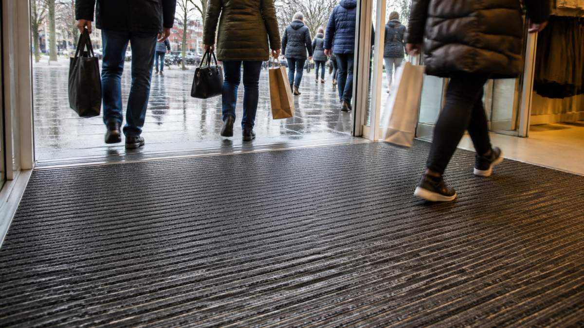 Gulvbelægning til butikkens indgangsparti: Sådan vælger du 2 Kunder med indkøbsposer træder ind på en slidstærk gulvbelægning til butikkens indgangsparti i regnvejr
